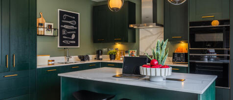 Modern kitchen with dark green cabinets, white marble countertops, and gold handles, decorated with