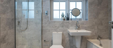 Modern bathroom with grey tiled walls, a walk-in shower, white toilet, wall-mounted sink, window sil