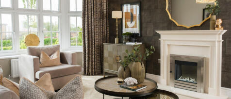 A modern living room with beige armchairs, a fireplace, large windows with patterned curtains, and e