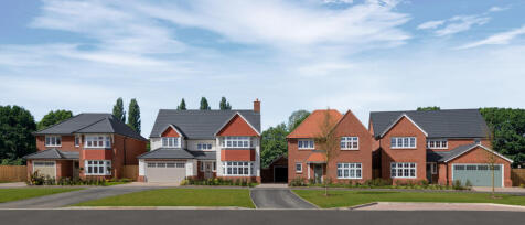 A row of modern detached brick houses with grey roofs under a blue sky and green trees in the backgr