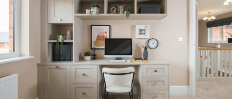 Modern home office with built-in white desk, shelves, and decor including plants, framed art, and a