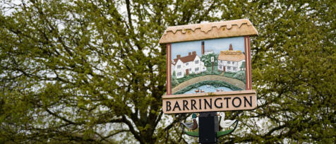 Barrington sign with painted houses, ducks, and greenery, set against a backdrop of green trees in a