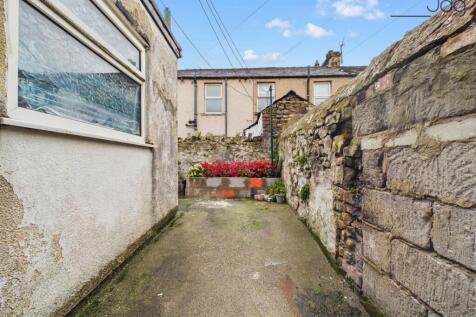 South-facing enclosed rear yard with a paved seating area, raised flower bed and ginnel access.