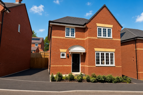 A modern red brick house with a black door and white-framed windows sits on a paved driveway