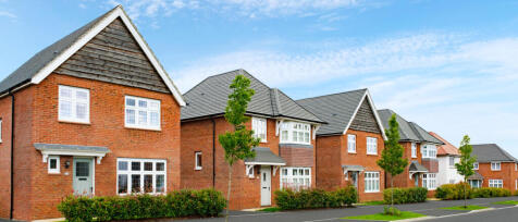 Row of modern red brick houses with grey roofs, small front gardens, and young trees along a clear s