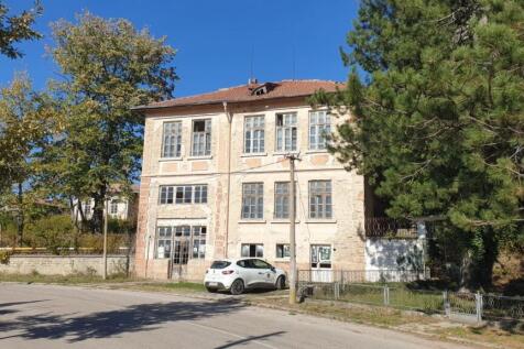Front view of the three-level former school building showing weathered facade and surrounding trees