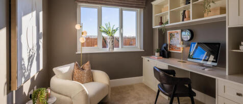 Modern home office with a white desk, black chair, beige armchair, and large window with potted plan
