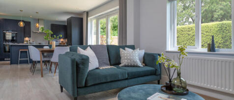 Modern living room with a teal sofa, decorative cushions, large windows with a garden view, and an o