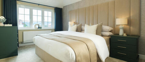 A neatly made double bedroom with a large window, beige headboard, and dark green side tables with l