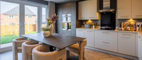 Modern kitchen with white and grey cabinets, wooden flooring, and a dining table with cushioned chai