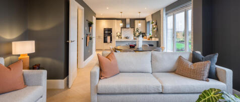 Modern furnished living room with beige sofas, colourful cushions, and large windows overlooking a g