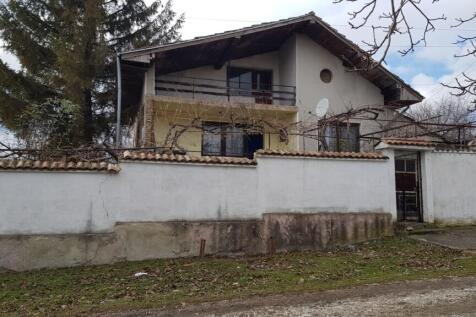 Front facade of a two-storey Bulgarian house with balcony and white garden wall