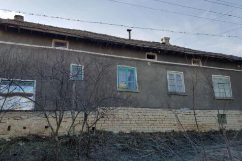 Front side of a Bulgarian village house showing stone foundation and plastered walls with multiple windows