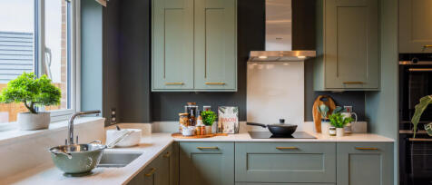 Modern green kitchen with white countertops, potted plants, and a large window providing natural lig