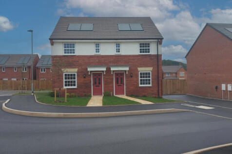 A newly built semi-detached house with red doors and white windows stands on a paved road in the for
