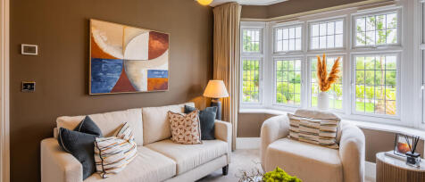 Bright living room with beige sofa, armchair, colourful cushions, large bay window, and modern decor