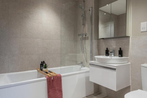 Family bathroom with a nice sized bath, sink, toilet and a mirror. White and grey tones