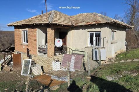 Side perspective of a Bulgarian rural house showing stone foundation and brick walls under clear blue sky