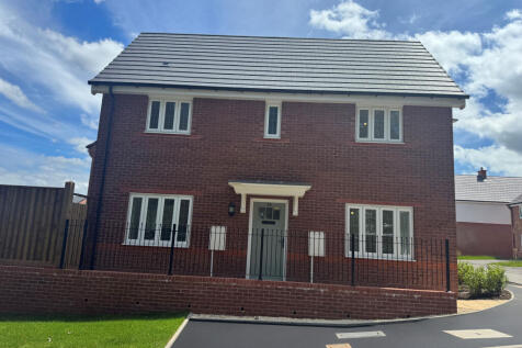 A modern red brick house with white-trimmed windows stands behind a low brick wall and black fence