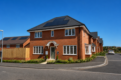 A modern brick house with solar panels on its roof sits in the foreground