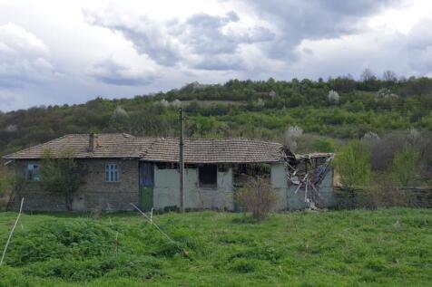 Side perspective of an old house showing a partially collapsed roof and green field with hills in the background.