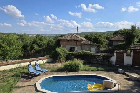 Outdoor swimming pool with clear blue water and two blue double sun loungers set on stone paving near garden greenery.