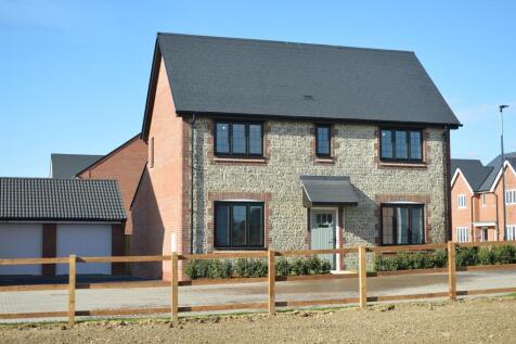 A modern stone and brick house with a dark roof stands behind a wooden fence in the foreground