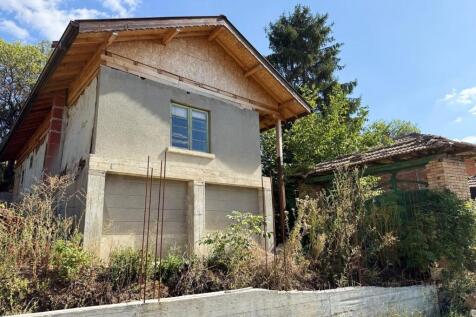 Exterior view of an old Bulgarian house showing new roof construction and chimney against a clear sky.
