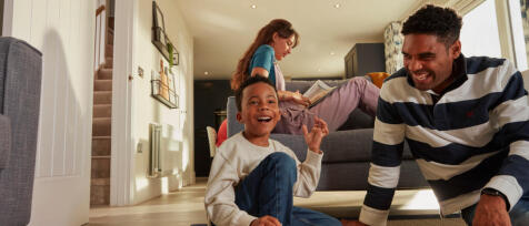 Family enjoying fun time indoors, with a boy smiling on the floor, a woman reading on the sofa, and