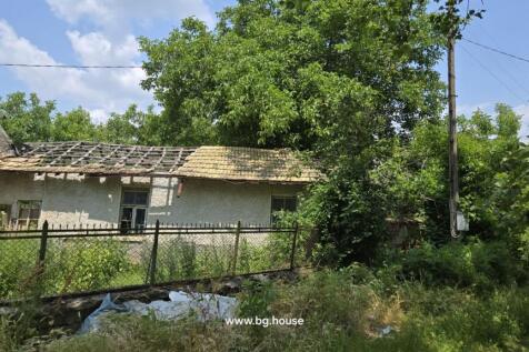 Garden space enclosed by a fence with trees and an old building featuring a damaged roof in the background.