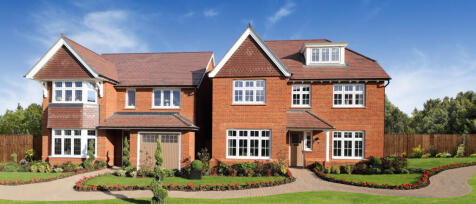 A large red-brick modern house with white-framed windows, front garden, and a driveway, under a blue