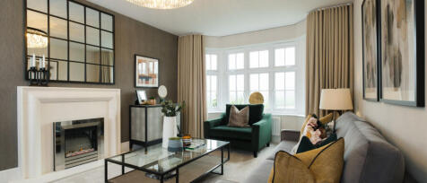 Modern living room with large bay window, grey and green furnishings, decorative cushions, and artis