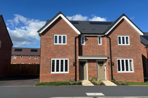A pair of modern red-brick semi-detached houses with white-framed windows stand under a blue sky wit
