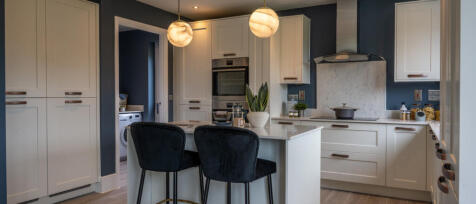 Modern kitchen with white cabinets, a centre island, black chairs, and a blue accent wall, illuminat