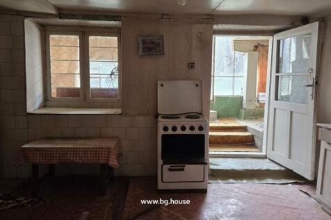 Room with a kitchen stove, a table, cupboards, and a door leading to a porch area with windows.