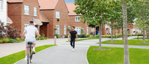 Two men in casual clothes walk and cycle along a winding path in a modern residential estate with re