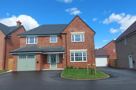 A modern brick house with a green garage door sits on a paved driveway in front of a bright blue sky