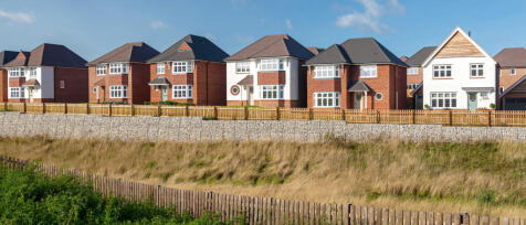 Modern detached houses with brick and white facades, set behind wooden fences on a sunny day with a