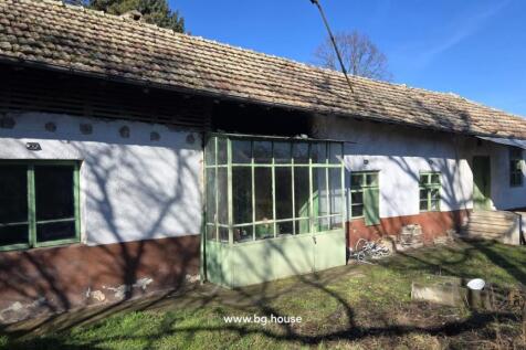 Front view of a traditional Bulgarian house with white and brown walls, green framed windows, and a tiled roof.