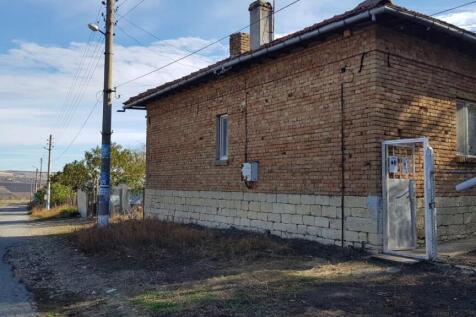 Side perspective of the two-storey brick and stone house showing metal gate and adjacent rural road