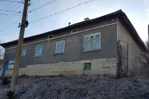 Side perspective of the house showing stone foundation and plastered walls with several windows and a blue door