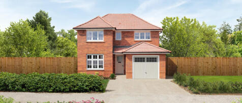 Modern two-storey red brick house with a garage, surrounded by trees and a wooden fence, under a cle