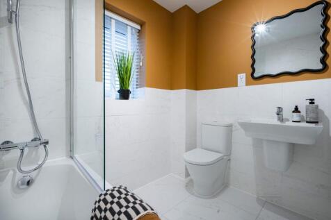 A modern bathroom features a bathtub with a glass enclosure in the foreground, and a toilet, sink