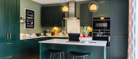 Modern kitchen with dark green cabinets, white marble island, and sleek black appliances under warm
