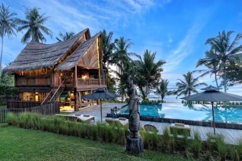 A tropical cabin with a thatched roof is set besid