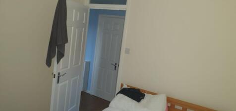 Compact bedroom with a simple wooden bed, neutr...