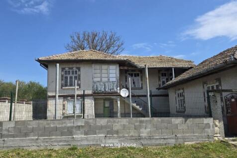 Front view of a traditional Bulgarian house showing tiled roof, multiple windows, and a fenced yard