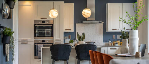 Modern kitchen with white cabinets, dark blue walls, and a marble backsplash, decorated with plants