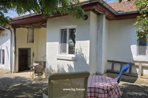 Outdoor courtyard showing white plaster walls, tiled roof, and a small table with chairs under tree shade.