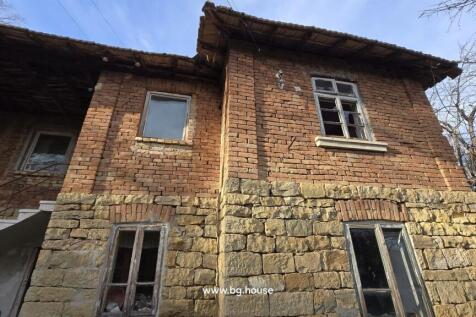 Front facade of a traditional two-storey house with stone and brick walls, multiple windows, and a white staircase leading to the upper floor.